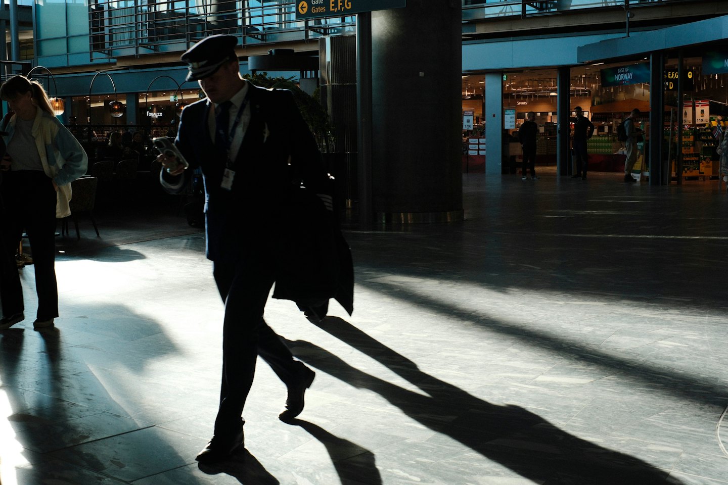 Ein Pilot in Uniform geht mit seinem Handy durch das Flughafenterminal.